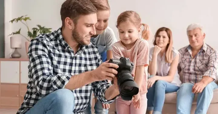 Photographer showing a little boy and girl photos on his camera, while the children's parents sit in the background