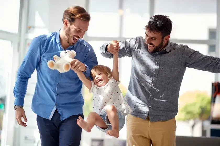 Two husbands lift up their toddler daughter. Marriages and civil unions each offer certain legal rights and privileges, but they don’t carry the same weight in every scenario.