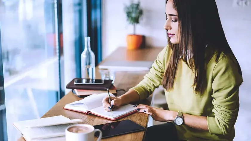 Woman writing in notebook by window