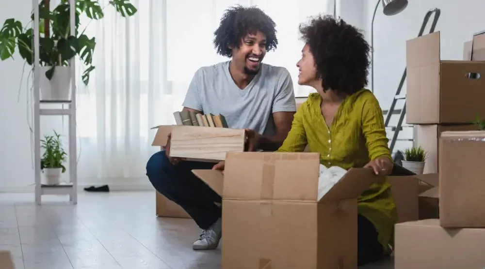 A man and a woman smile at each other while they open moving boxes. Married couples in Arizona have equal ownership of property obtained during the marriage.