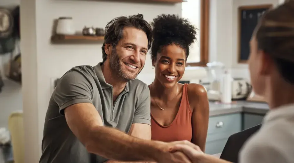 A man shakes hands with a female prenuptial attorney as the woman he is engaged to sits next to him.