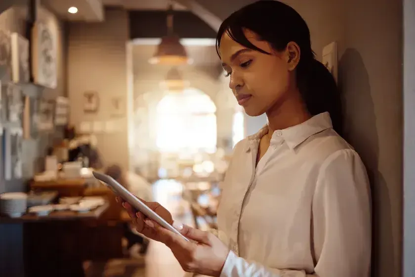 The owner of a restaurant leans against a wall in a hallway off of the dining room and reads about percentage leases on her iPad