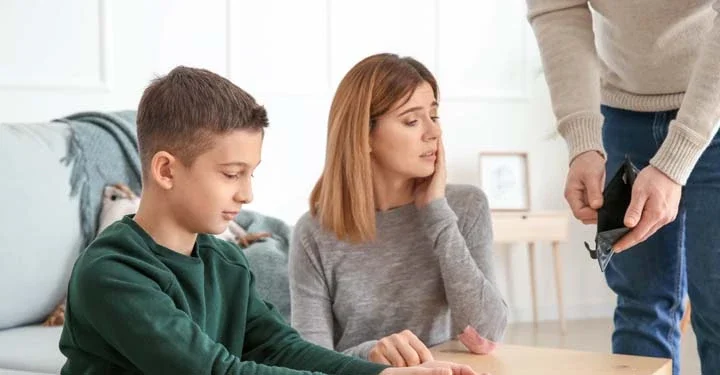 A mother and child sitting on the floor in front of a coffee table. An unemployed man is showing her an empty wallet despite needing to make a child support payment.