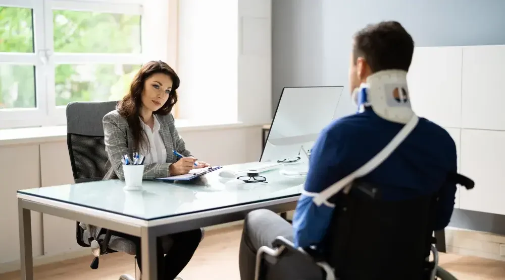 A rideshare accident attorney sitting across from a man in a neckbrace discussing the compensation he can receive for an accident