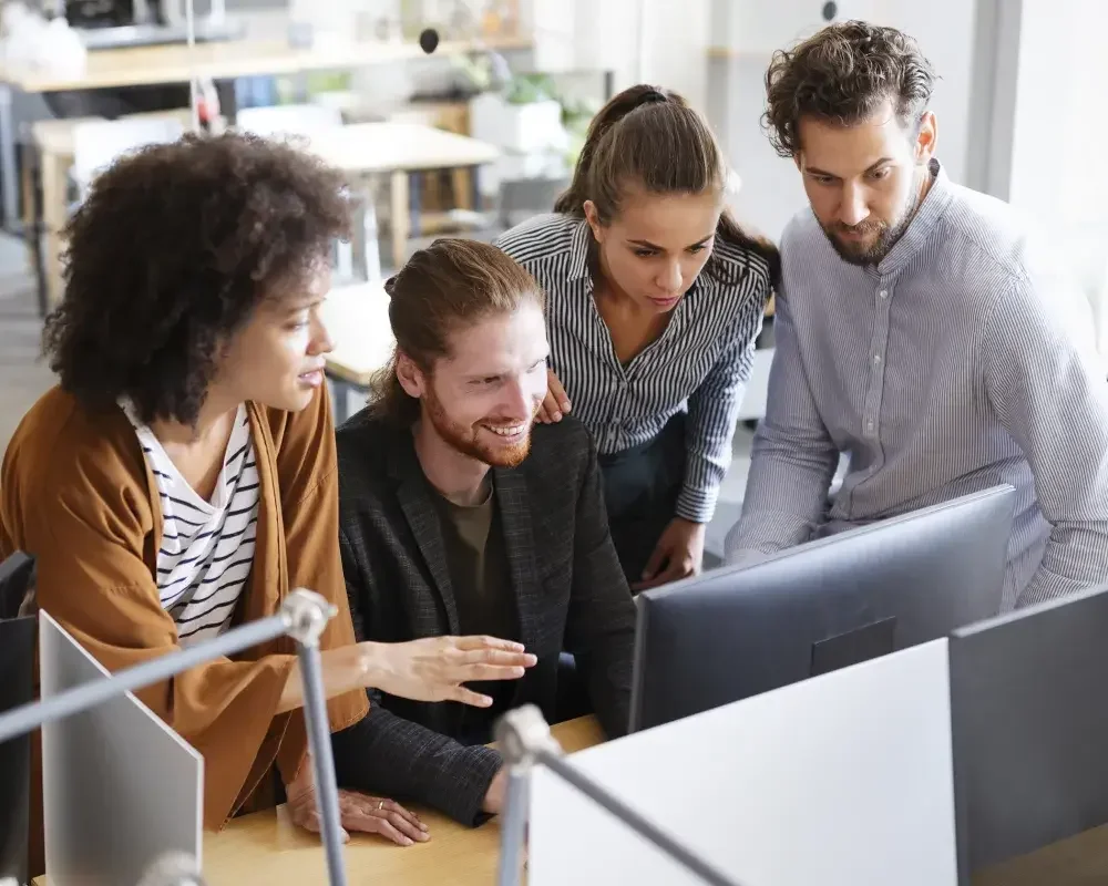 Employees gather around a desktop to look at designs on a screen. Not all companies have to file a report under the Corporate Transparency Act: FinCEN lists 23 types of exempt entities.