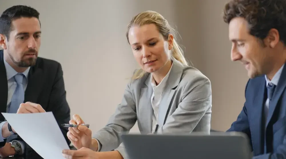 Two men and a woman sit at a table, looking over paperwork for a modified gross lease