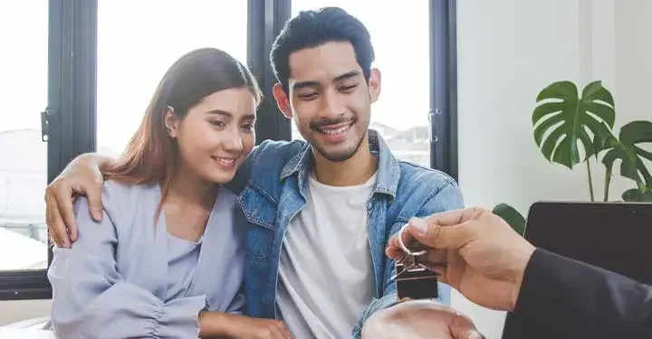 Couple given keys to home in front of windows and plant