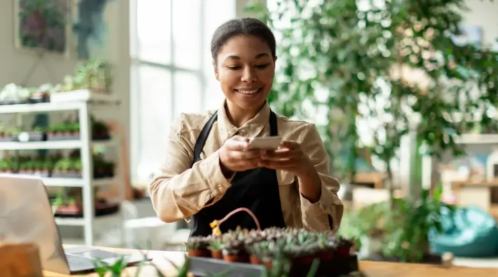 A woman takes a photo of a plant with her phone. Part of starting a landscaping business is choosing the right business structure such as an LLC. 