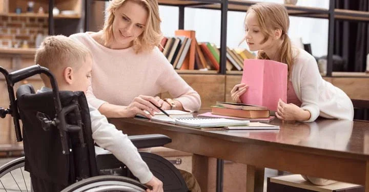 Woman, little girl, and little boy in a wheelchair working together at a table