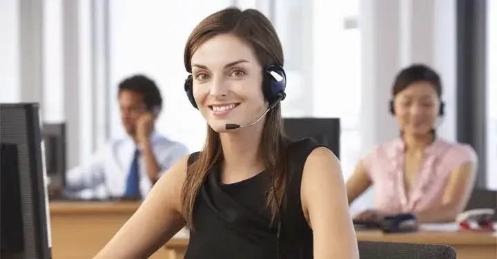 Woman in headset in front of computer smiles while listening to customer