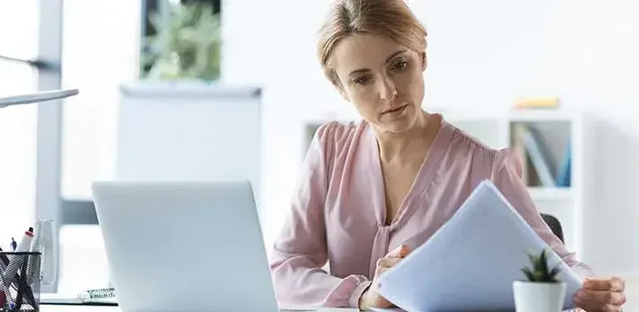 Businesswoman looking at a piece of paper next to her open laptop