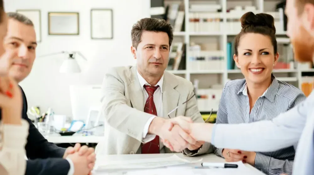 Office workers sitting around a table smile and introduce themselves. It's important for business owners to stay ahead of the FTC non-compete game where federal regulations are concerned.