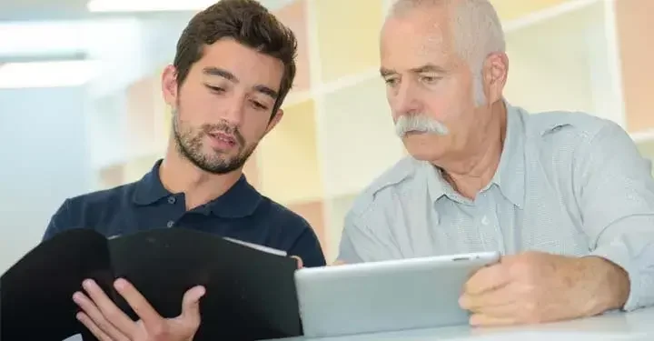 Young man with binder and elderly man with tablet comparing information