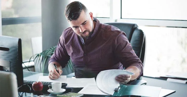 Man sitting in office at computer signing documents