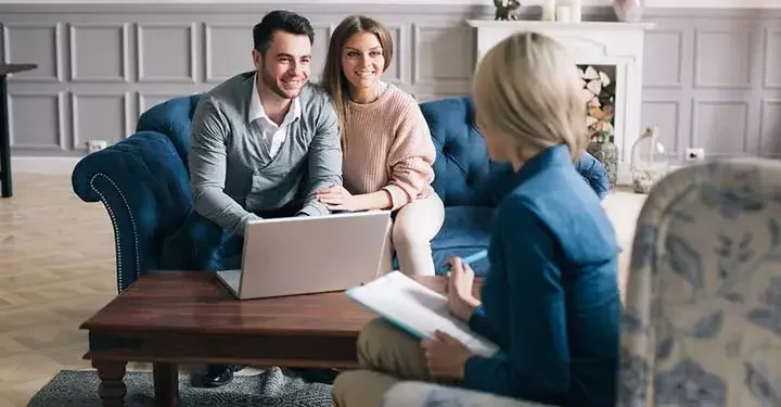 A happy couple sitting on a couch across from a woman with a clipboard