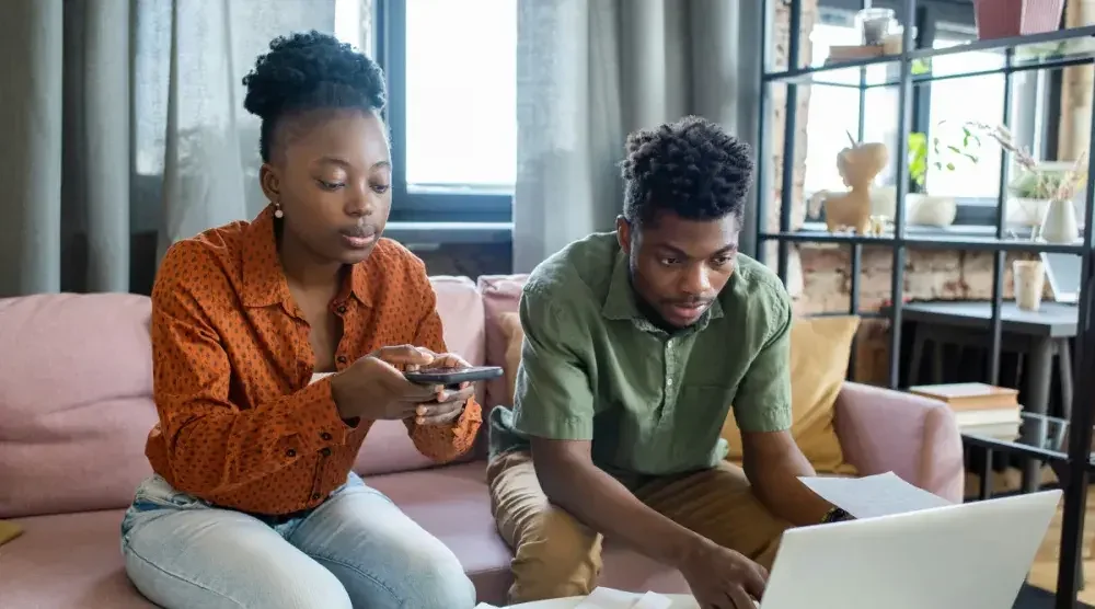 Two small business owners sit on a couch and go over their records before tax time. Tax deductions may be able to help small companies raise their profits.