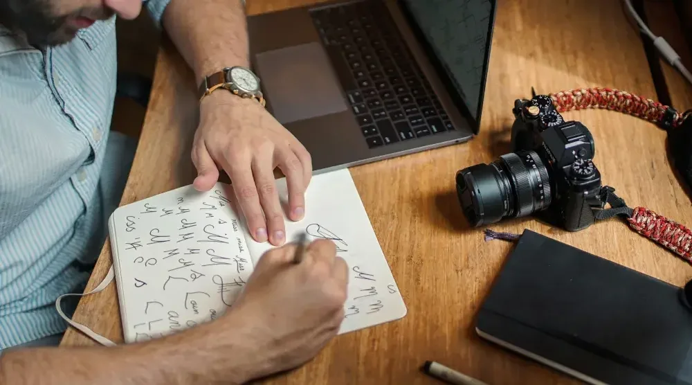 A photographer who is considering hiring a trademark attorney sits as his desk and designs his company's logo