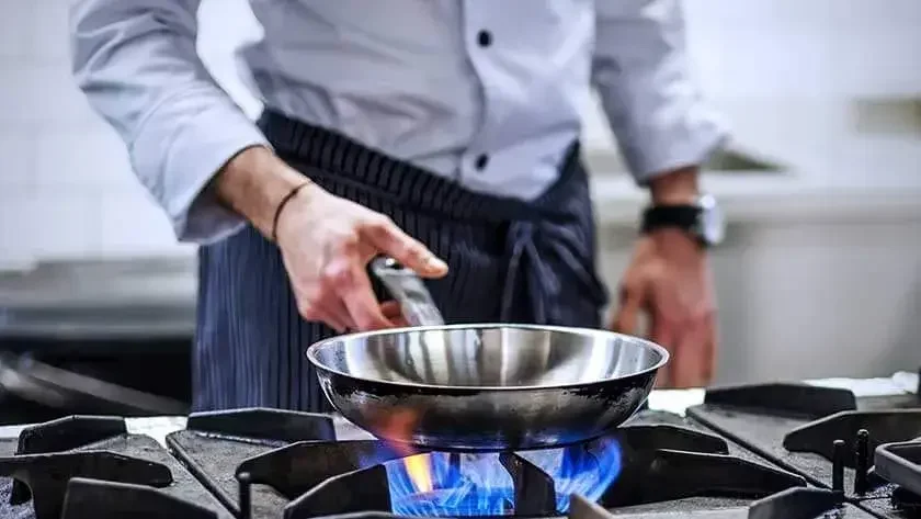 man-holding-pan-over-fire-stove in commercial kitchen