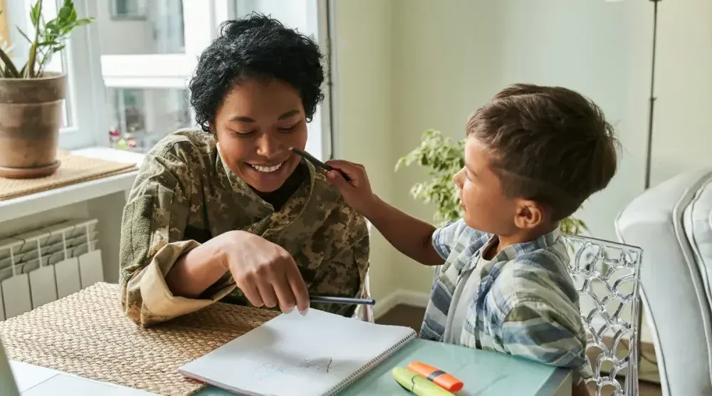 A child seated at a table pretends to paint on the face of a daycare worker as she tries to get him to concentrate on his lesson.