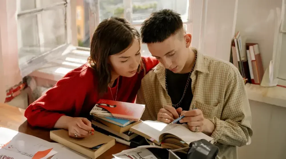 A newlywed couple—a young woman and a young man—sit at a desk as they look over their book collection. They chose to sign a postnup instead of a prenup. 