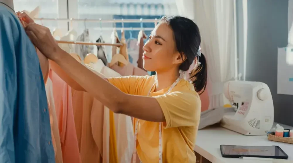 A woman who owns a tailor shop makes adjustments to a garment on a rack. Before she started her business in Oregon, she did a name search to ensure the name she wanted wasn't already taken. 