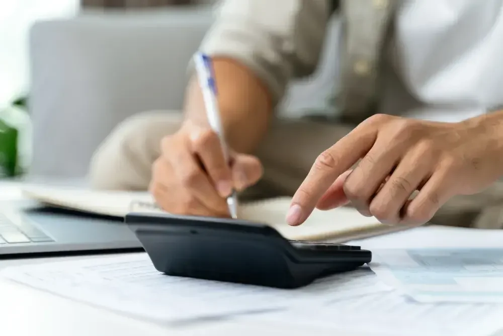 A person seated at a desk uses a calculator and takes notes while determining the IRS prinicipal business code for his small business.