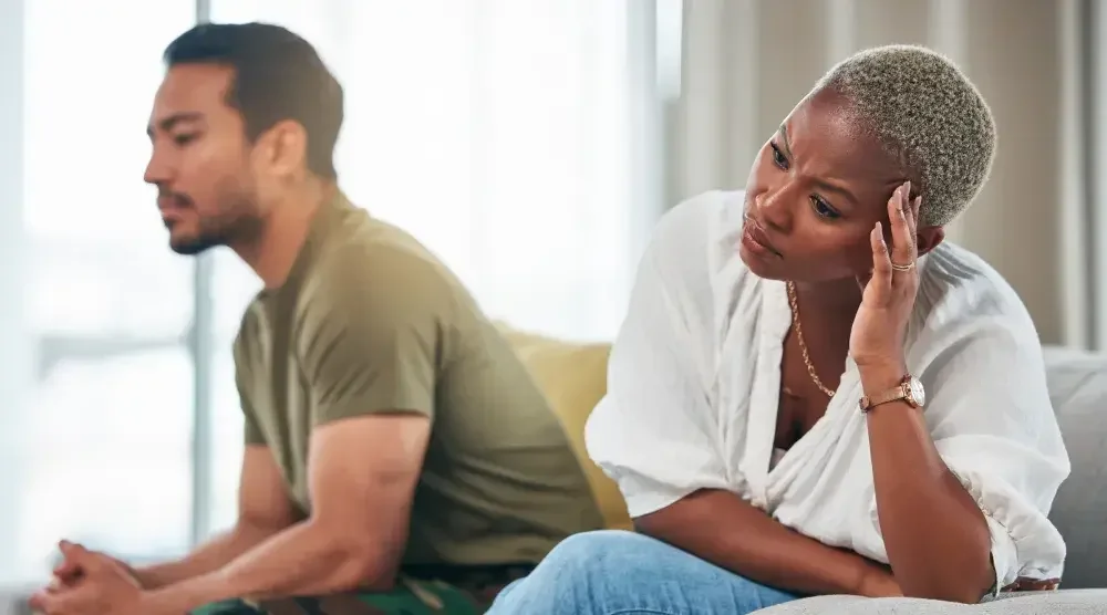 A husband and wife sit on the couch. The wife is clearly frustrated. Many spouses overlook signs that their wife is considering a divorce.