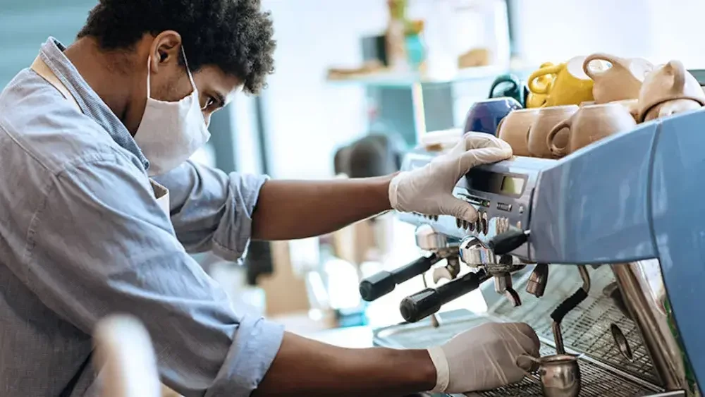 A coffee shop owner wearing a medical mask makes an espresso.