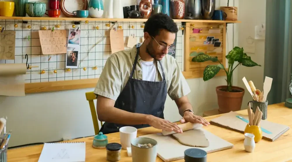 An Alaskan business owner sits in his pottery studio and rolls out some fresh clay on a workbench.