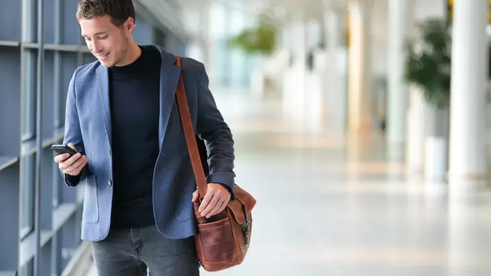 A man looks at his cell phone while boarding a flight for business travel. Business travel deductions fall into three categories: costs related to how you will get to your destination (travel), where you will stay (lodging), and what you will eat and drink when you are there and in transit.. 