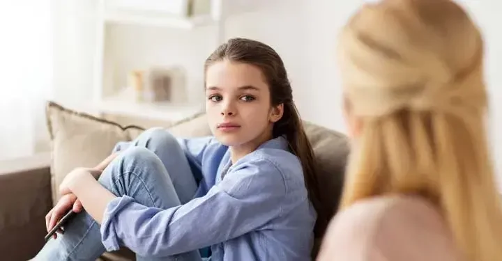 Little girl with long, brown hair sitting on a couch looking at a blonde woman