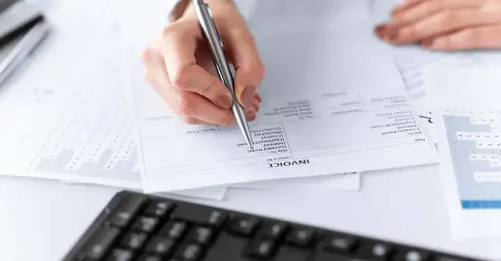 Person holding a silver ballpoint pen while looking over invoice