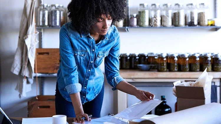 woman in blue shirt looking over paperwork in home office 