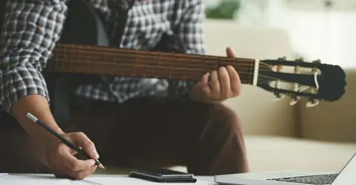 Man holding guitar writing with a pencil