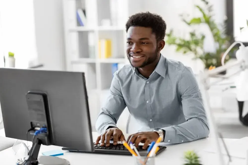 A man seated at a desk reads the screen of his computer while filling out documents to form his new business.