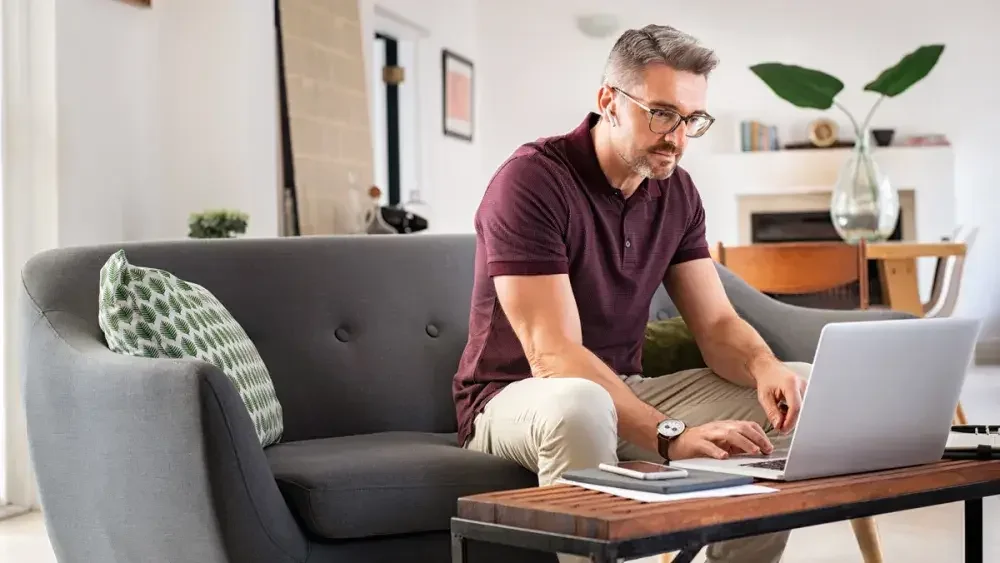 A man sitting on a couch in his living room fills out a last will and testament template online. His will is the cornerstone of a sound estate plan.