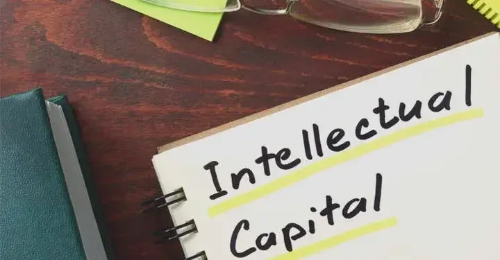 An open notebook with the words "Intellectual Capital" written inside next to a book and a pair of glasses