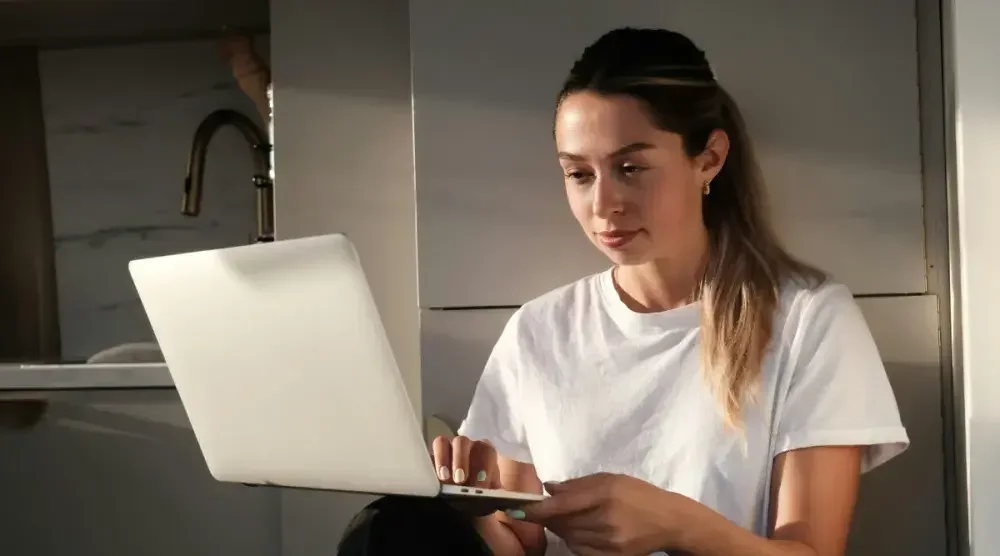 A woman in a white T-shirt and ponytail looks up executor duties on her laptop. Estimating how long it takes for the executor to pay beneficiaries partially depends on how quickly the executor files the will with the probate court