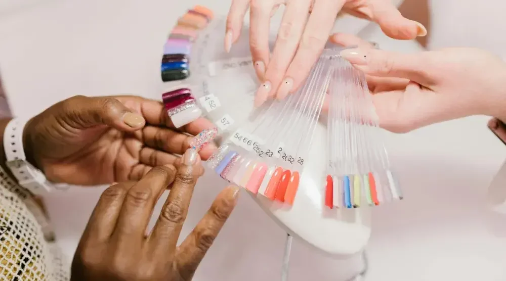 A nail technician holds out a fan of polish samples up to her client's hand.