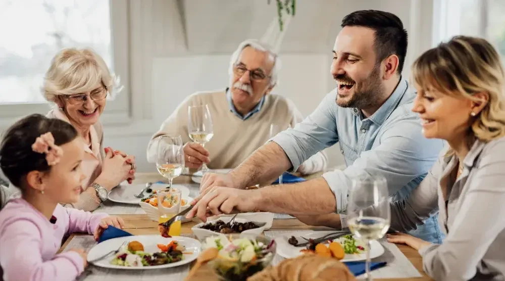 A young girl, her grandparents, and father and mother eat dinner after discussing per stirpes. In estate planning, per stirpes is a distribution provision for assets. 