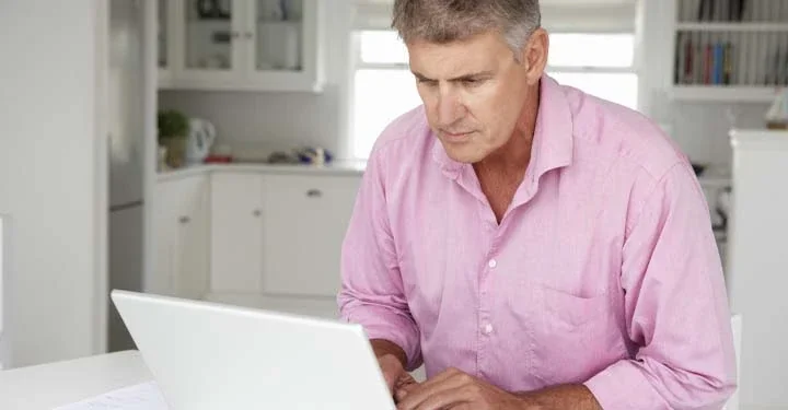 Man in pale pink button-down shirt using laptop