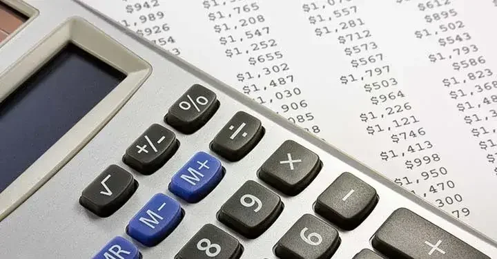 Calculator resting on piece of paper containing a list of amounts of money