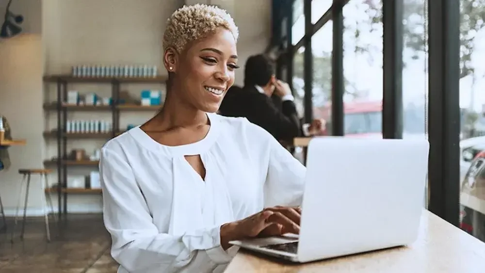 A woman sits at a cafe counter working on her laptop computer to set up an appointment with a financial advisor to create a trust.