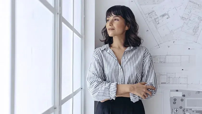 woman in striped shirt standing against a will with plans 